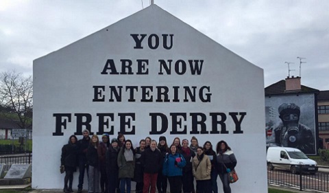 Students meet with Bogside Artist Tom Kelly in front of the famous Free Derry wall at Free Derry Corner, the site of the 1972 Bloody Sunday massacre in Derry.