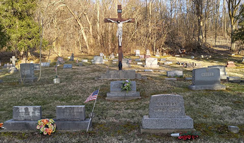 Buchtel Cemetery in Buchtel Ohio with crucifixion cross and stone with graves/headstones surrounding and woods in background