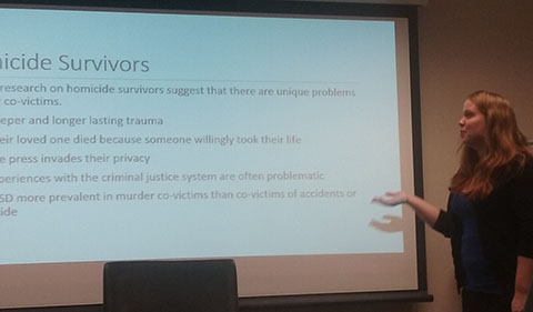 Lauren Wright standing to the side of a slide about Homicide Survivors teaching Sociology of Murder class at the University of Central Florida, Spring 2016