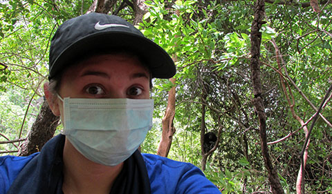 Nicole Wackerly wearing surgical mask in Senegal with Fongoli chimp Bo (adult male) in the background. Because humans are so closely related to chimpanzees, we wear masks when in close proximity as a precaution against disease transmission.
