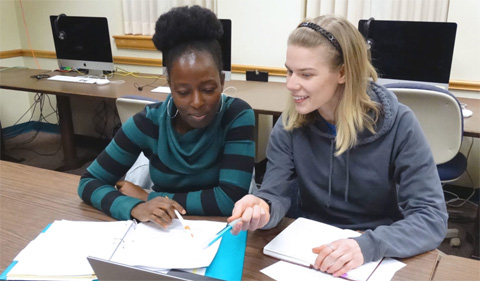 Francisca Lekey (left) and Anna Palmer (right) organize their research for the next phase of their thesis. They are shown here sitting at a table looking at their notes.