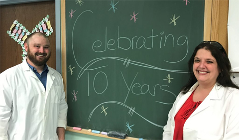 Ohio University Genomics Facility celebrates 10th anniversary, with Bill Broach and Rachel Yoho. 10th anniversary is written on the chalkboard.