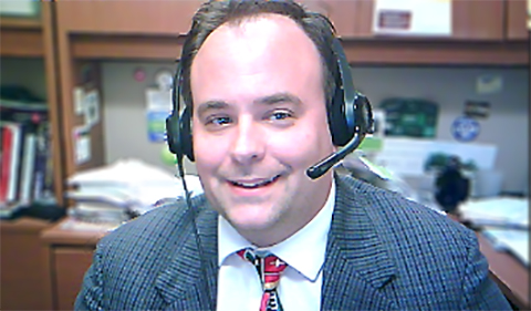 A smiling Scott Powell at an office desk with headset on