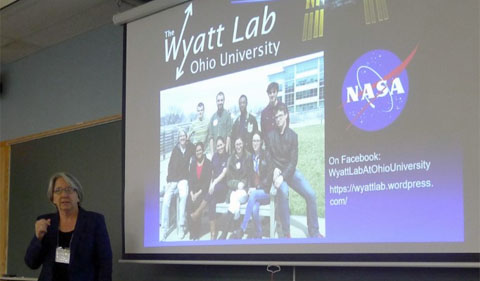 Dr. Sarah Wyatt talks about her experiment on the International Space Station, with slide showing NASA logo and group photo of her students.