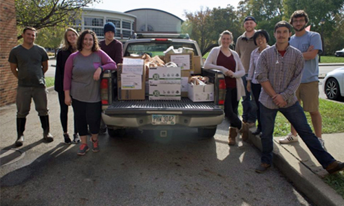 Students take food drive donation to Good Works, shown here is pickup truck loaded with boxes of donated food and surrounded by nine student volunteers.