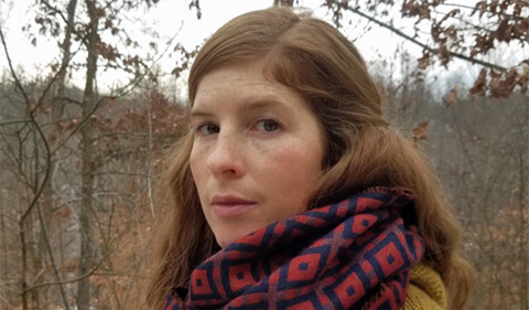 Madeline ffitch, wearing winter sweater and scarf and stading in the woods