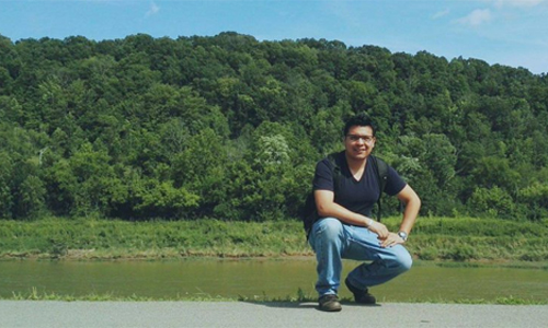 Ricardo Molina Herrera, wins first place in OPIE Writing Contest, shown here kneeling by a lake.