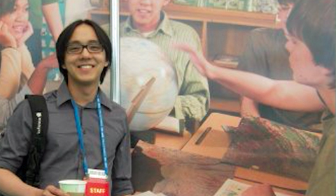 Kenny Ling at a conference, standing in front of a poster illustrating how important geography is.