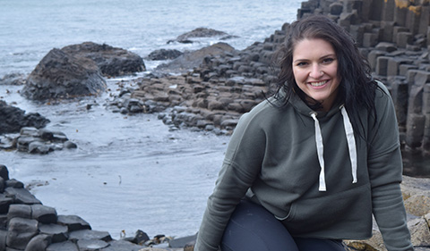 A smiling Abigail Guerra seated on rocks at waters edge on the Giant's Causeway on the Antrim coast of Northern Ireland in March 2018.