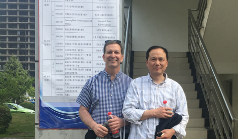 Dr. Christopher France with his host, Professor Ming Zhu, standing in front of advertising banner.