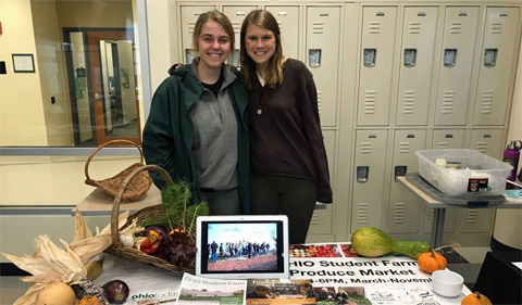 Students, Joy Kostansek and Rachel McDonald, stand and pose for a photo behind the Food Studies table.