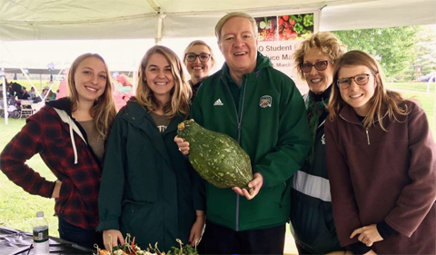 President M. Duane Nellis at the College of Arts & Sciences Homecoming tent holding a giant Hubbard Squash grown at the OHIO Student Farm. From left: Allison Paolucci (Plant Biology Food Studies Graduate Assistant), Joy Kostansek (Food Studies Graduate Assistant and Sociology), Jen Vanderman (B.S.S.), President Nellis, Dr. Theresa Moran (Director of Food Studies), and Rachel McDonald ( Food Studies Student Assistant).