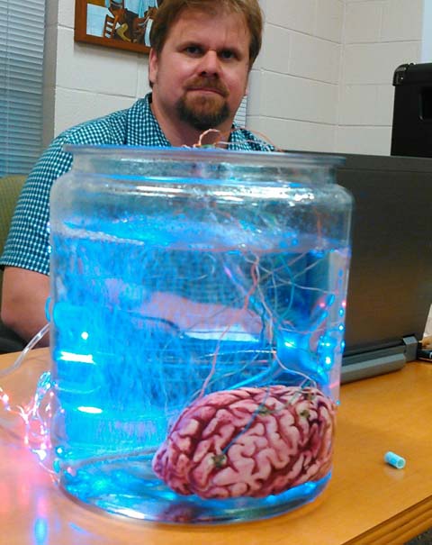 Michael Veber, portrait with human brain in jar in front of him.