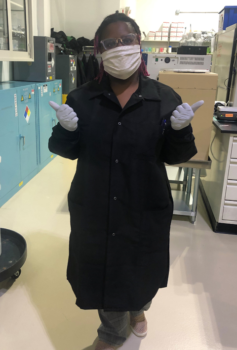 Demi Reed in the lab, full gown, face mask and gloves.