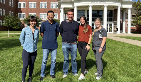 Drs. li Xu and Mark Gibson with students, posing outside Grover Center