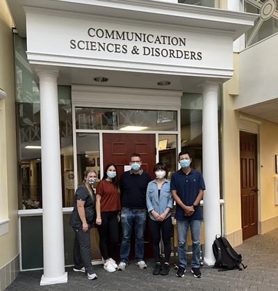 Mark Gibson, Li Xu and students pose under doorway labeled "Communication Sciences & Disorders